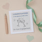 A Nephew and wife to be engagement congratulations card with two celebratory glasses design, placed on a neutral background with a pen, ribbon, and cut-out hearts.